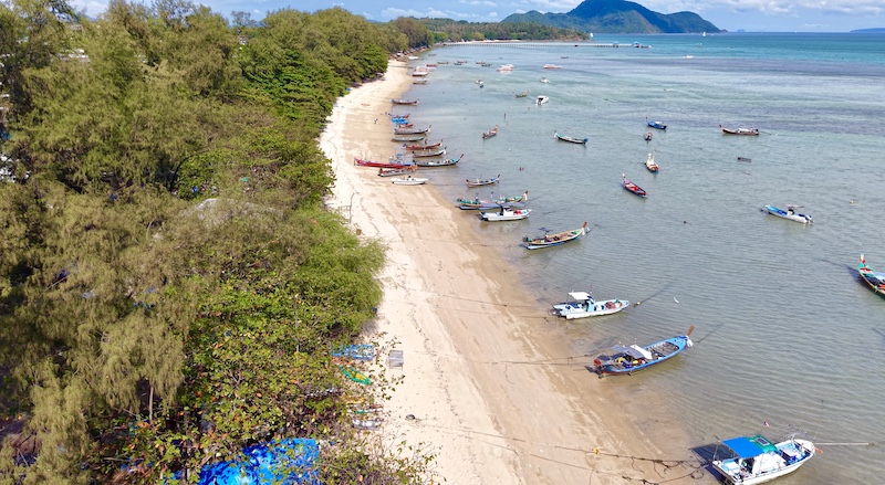 Scenic view of Rawai Beach in Phuket, Thailand, with traditional longtail boats and palm trees.